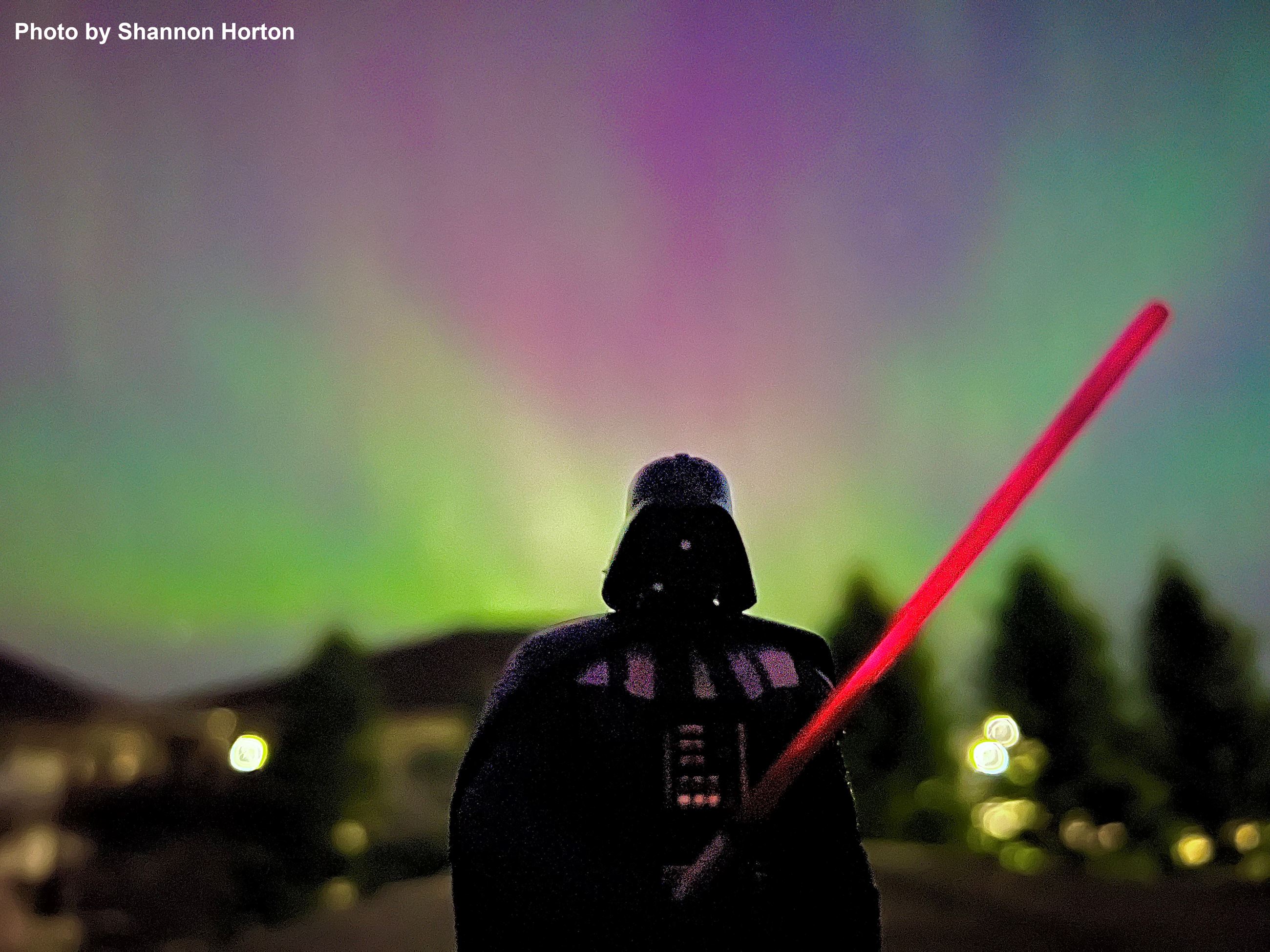 A toy figure of Darth Vader shown in the foreground with the Northern Lights in the background. 