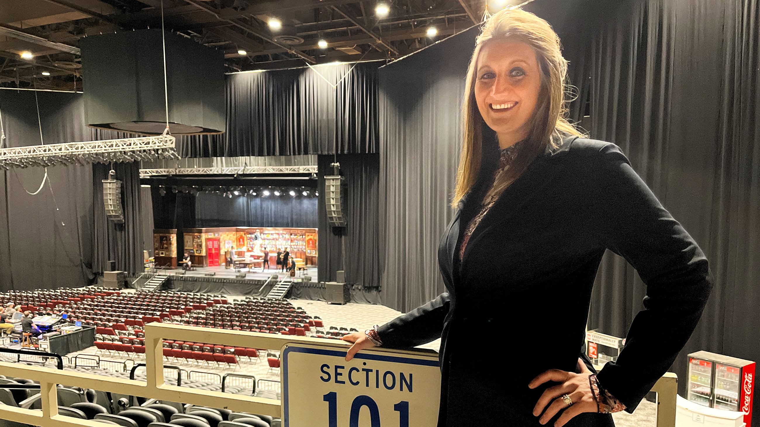 A woman standing in front of a railing in a large event space. 