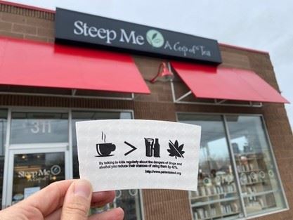 A coffee sleeve designed by the student committee held in front of a coffee shop. 